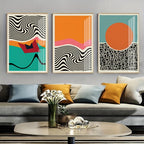Three abstract art pieces on a wall above a gray sofa with colorful cushions.