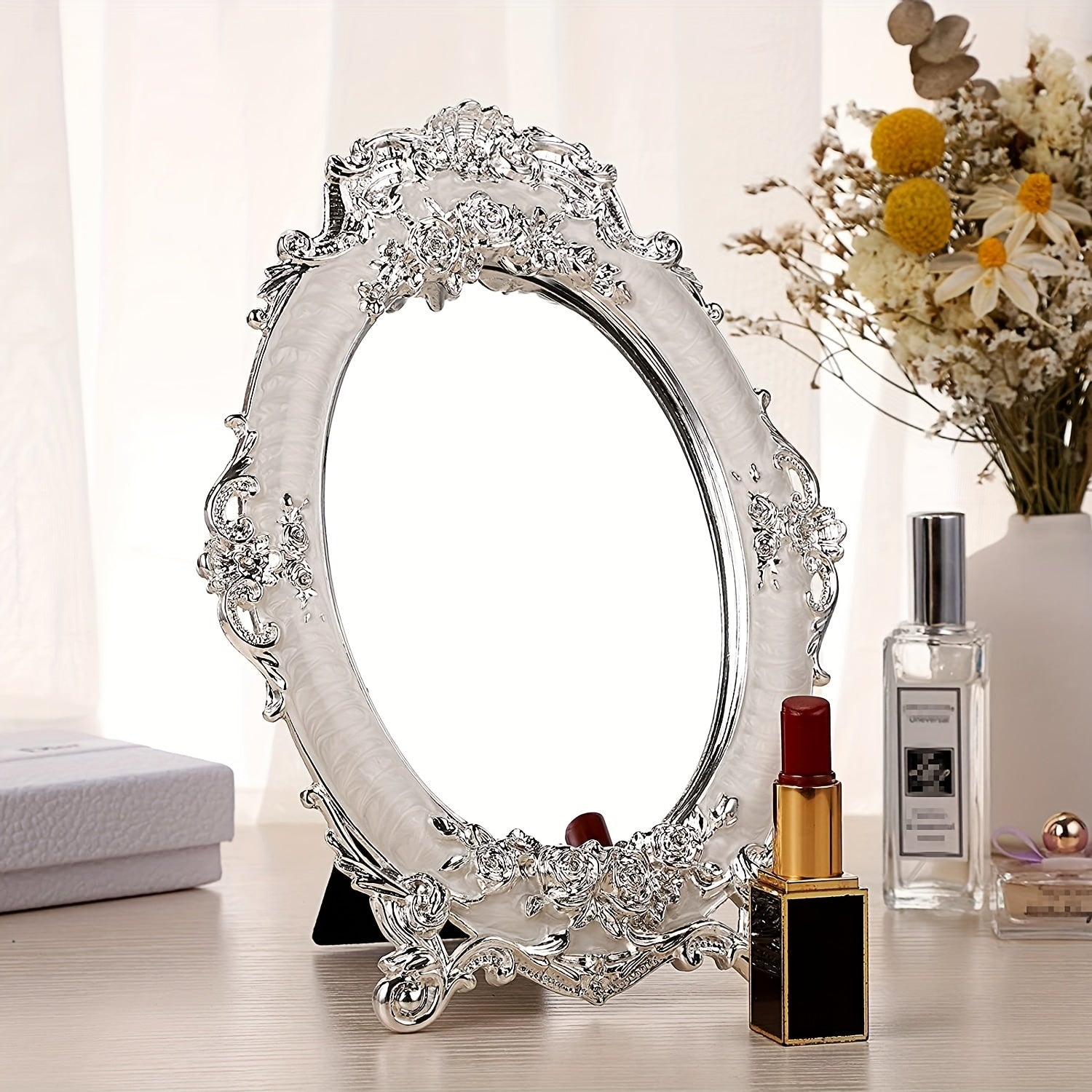 Decorative oval mirror with intricate design on a surface with makeup items.