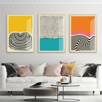 Three abstract art prints on a wall above a white sofa with decorative pillows.