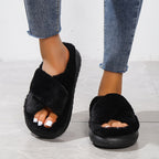 Black fuzzy slippers worn with blue jeans on a light gray floor.
