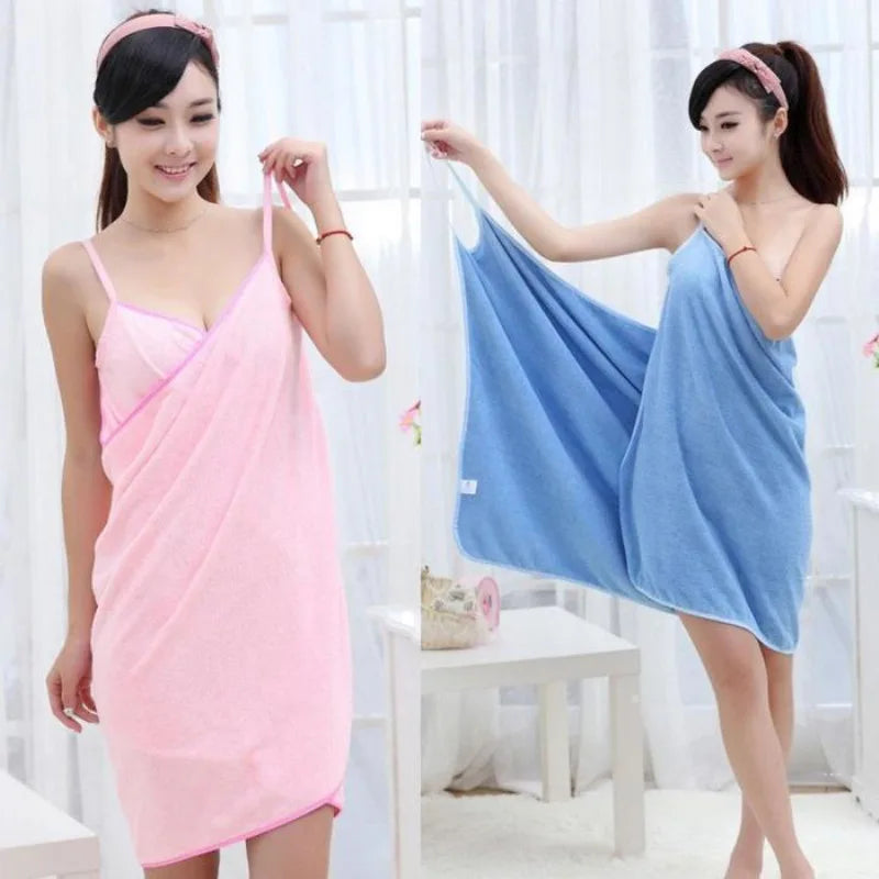 Two women wearing pink and blue towel dresses in a room with white curtains.