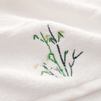 Embroidered design of branches and leaves on a white fabric background