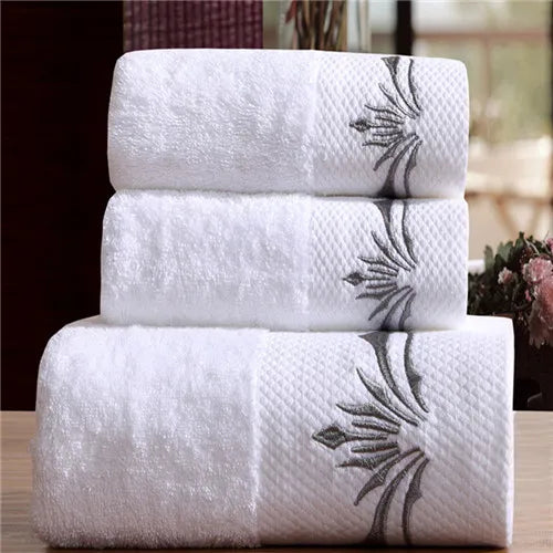 Three white towels with floral embroidery stacked on a wooden surface.