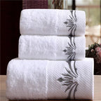 Three white towels with floral embroidery stacked on a wooden surface.