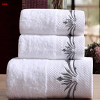 Three white towels with floral embroidery stacked on a wooden surface.