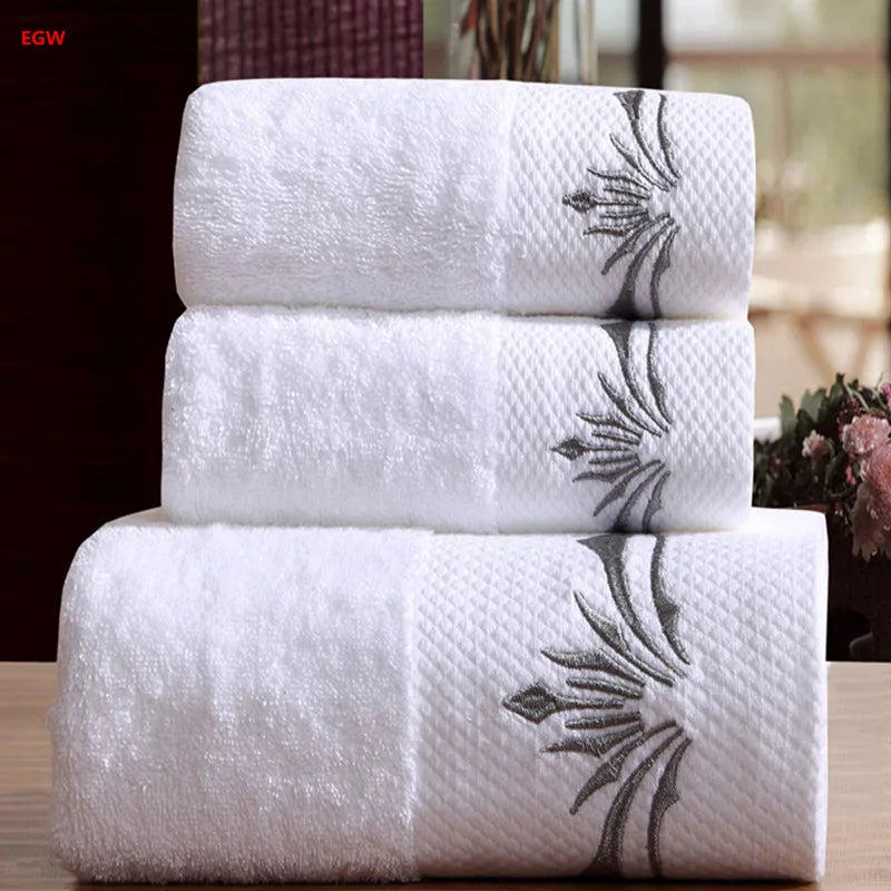 Three white towels with floral embroidery stacked on a wooden surface.