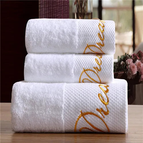 Three white towels with gold embroidery on a wooden surface