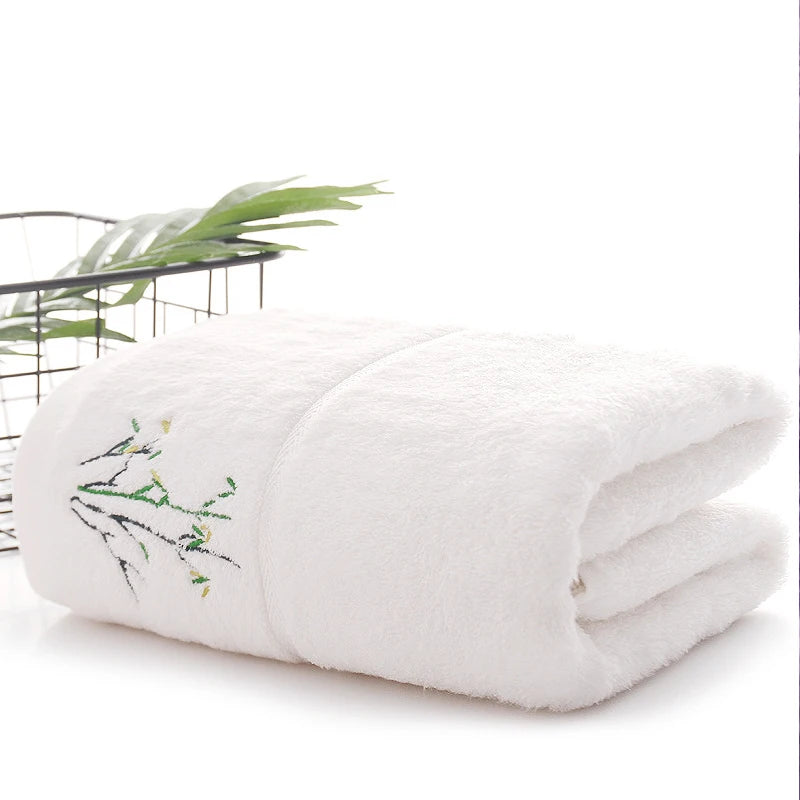 Folded white blanket with embroidery on a white surface with a plant in the background