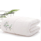 Folded white blanket with embroidery on a white surface with a plant in the background