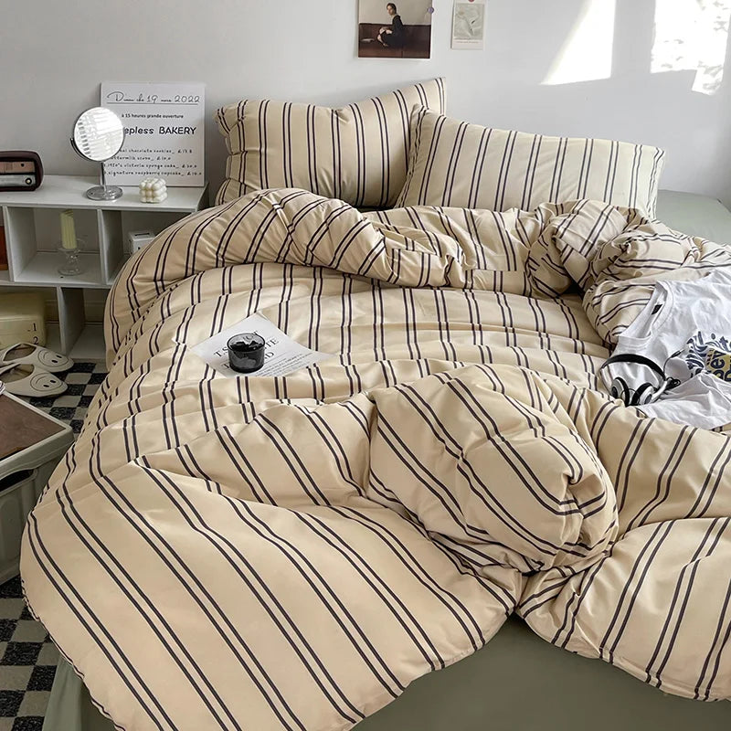 Beige and brown striped bedding set on a bed in a room with a small table and decor items.