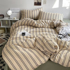 Beige and brown striped bedding set on a bed in a room with a small table and decor items.