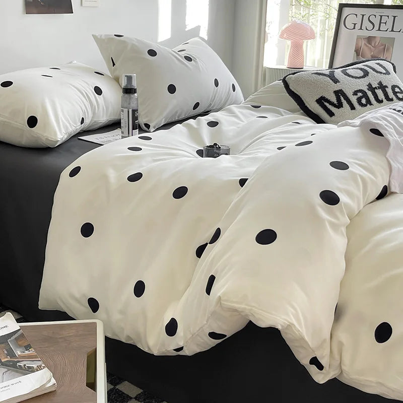 Polka dot bedding set on a bed with pillows and a lamp in the background.