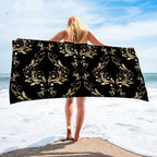 Person holding a black and gold patterned towel on a beach