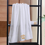 White towel with a gold crown logo on a black towel rack against a wooden wall.