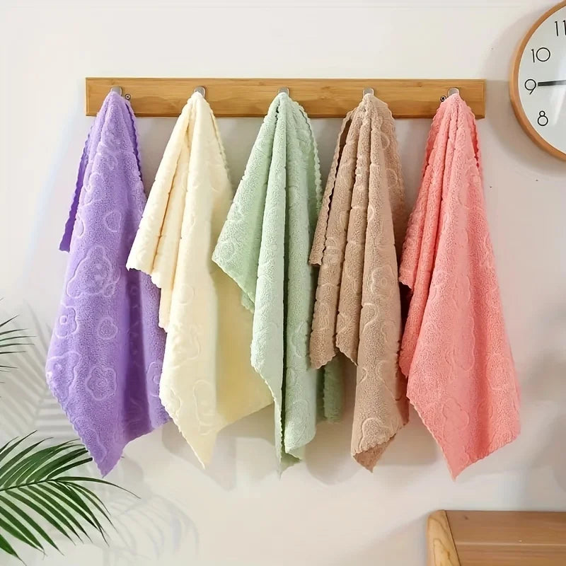 Five colorful towels hanging on a wooden rack against a white wall with a clock.