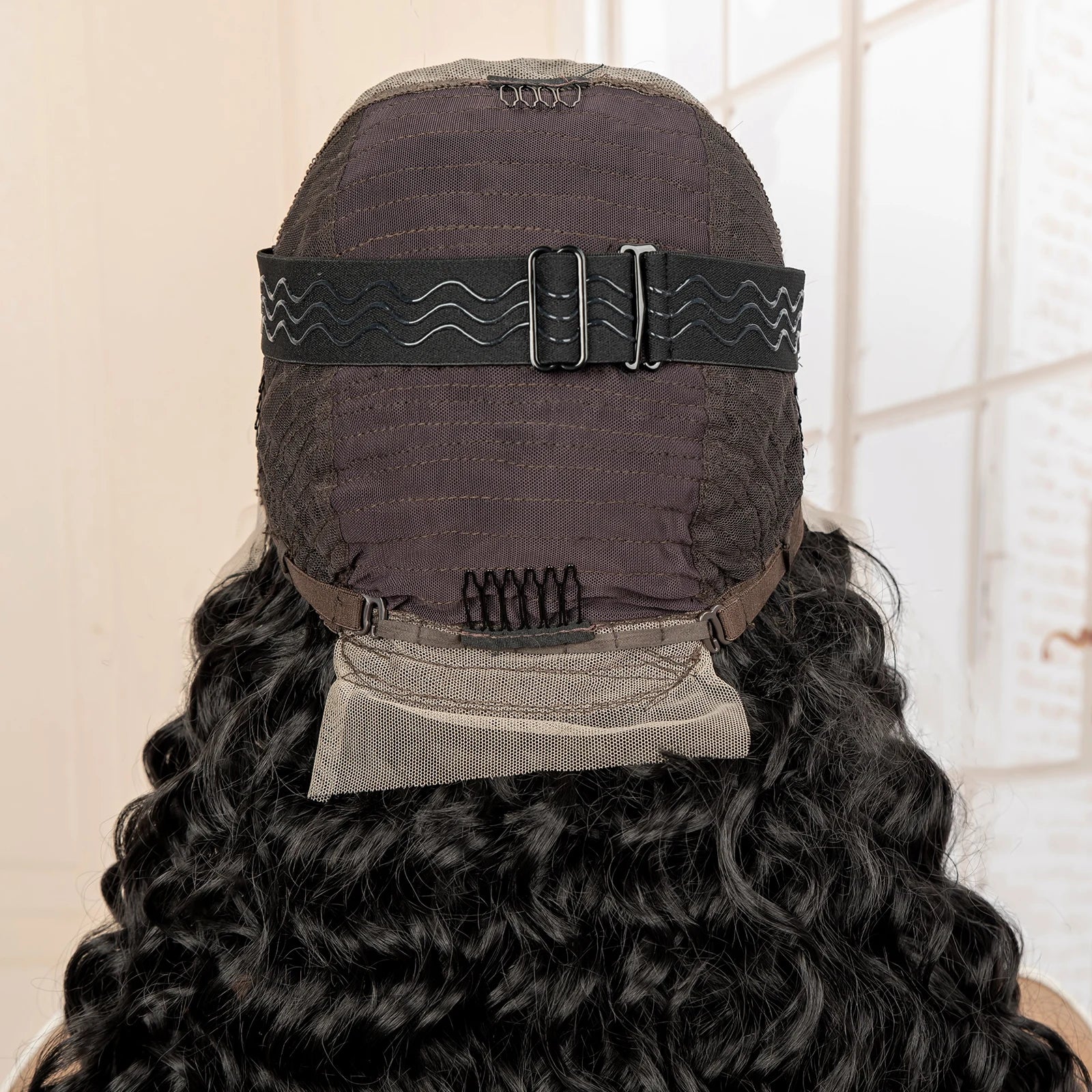 Back view of a wig with a black cap and adjustable straps on a neutral background