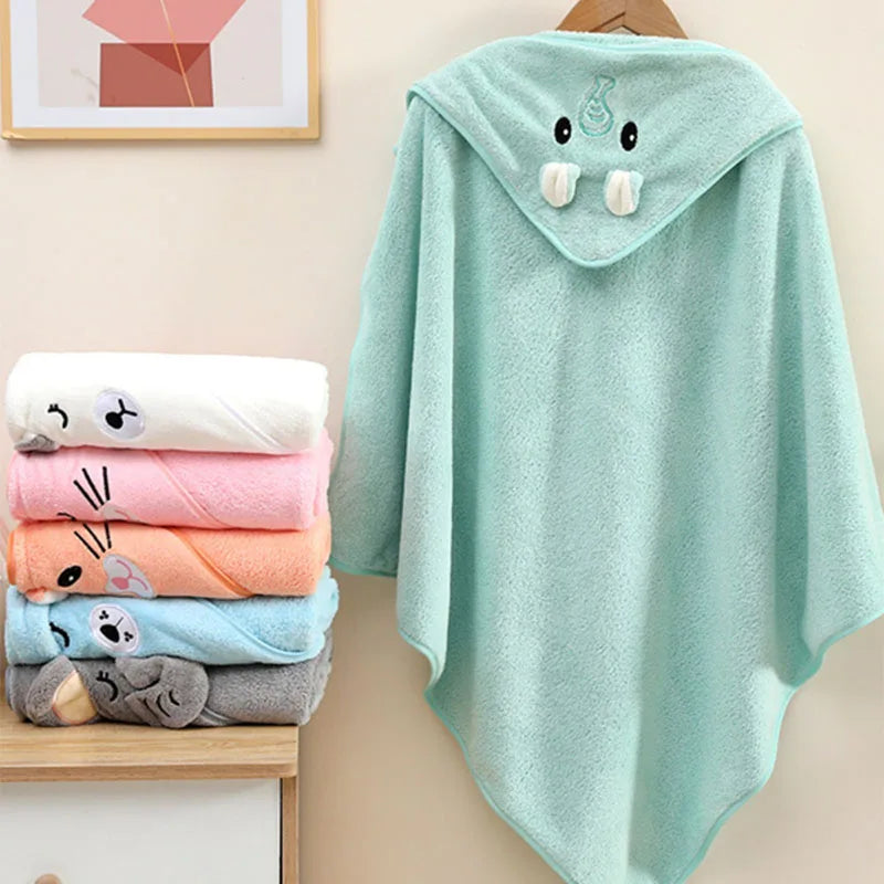 Stack of colorful baby towels with a green hooded towel featuring cartoon face design on a beige surface.
