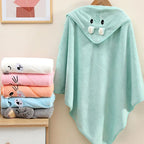 Stack of colorful baby towels with a green hooded towel featuring cartoon face design on a beige surface.