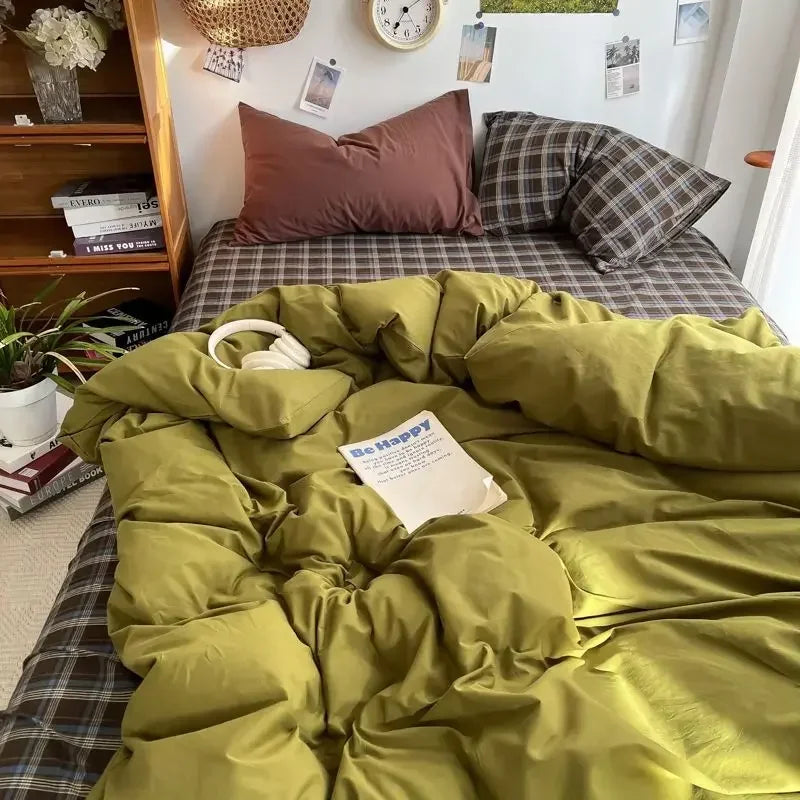 Bed with green comforter, plaid blanket, and pillows in a cozy room.