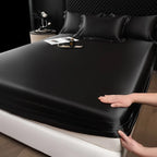 Black satin sheet being fitted onto a bed with a person's hands visible.