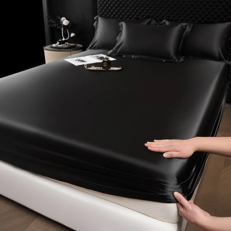 Black satin sheet being fitted onto a bed with a person's hands visible.