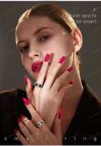 Woman with pink nails and rings, wearing a black top against a dark background.