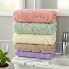 Stack of five colorful towels on a kitchen counter with a tiled wall and faucet in the background.