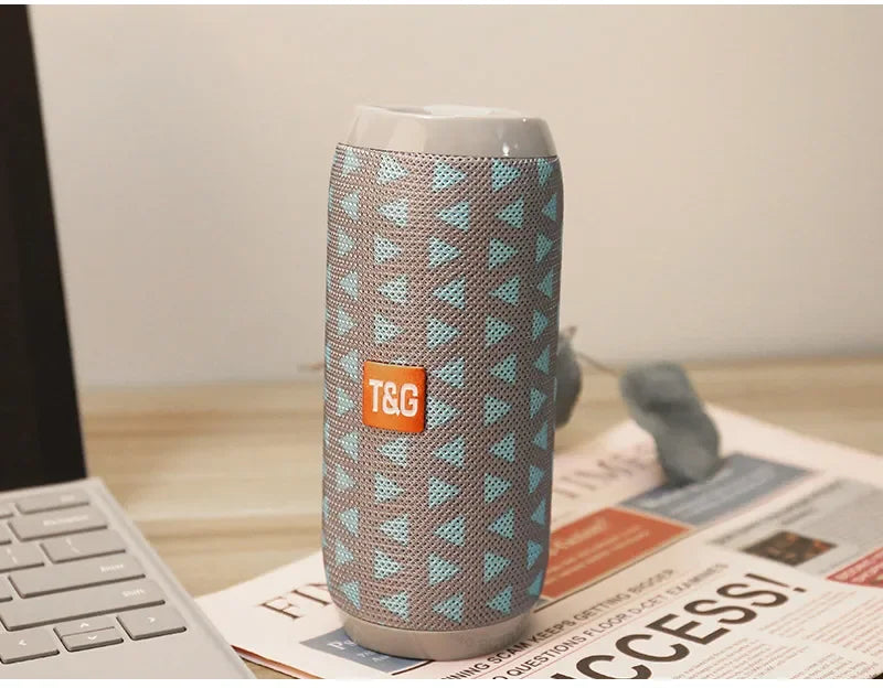 Tumbler with a pattern and TGG logo on a desk with a laptop and newspaper.