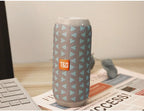 Tumbler with a pattern and TGG logo on a desk with a laptop and newspaper.