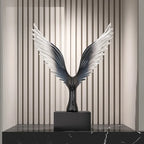 Decorative sculpture with wing-like design on a black platform against a striped wall.