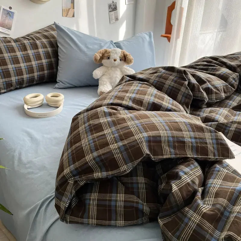 Bed with plaid comforter, pillows, and a teddy bear in a bedroom setting.