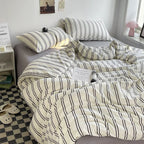 Striped bedding on a bed in a room with a window and small table.