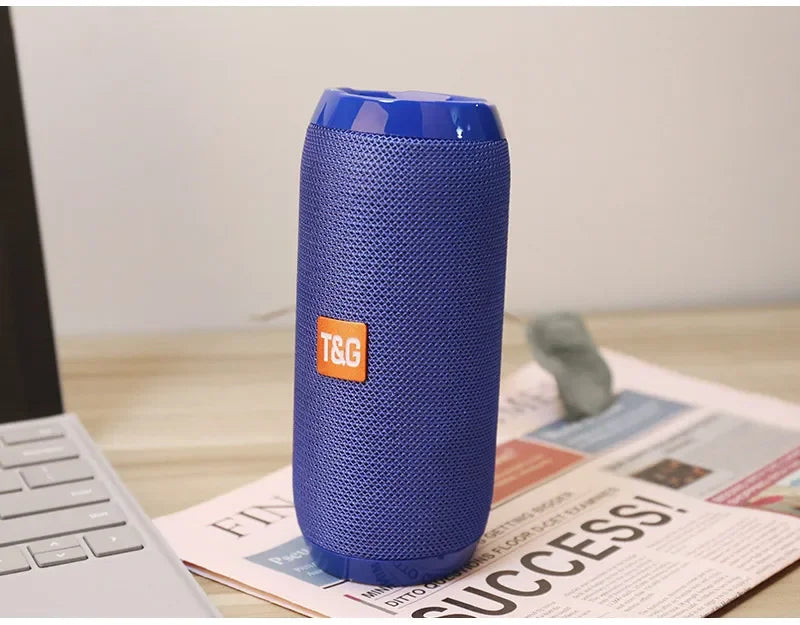Blue portable speaker with T&G logo on a newspaper and laptop