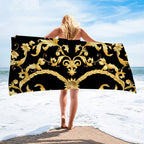 Person holding a decorative towel with gold patterns on a beach