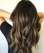Person with long, wavy hair with brown and blonde balayage on a plain background