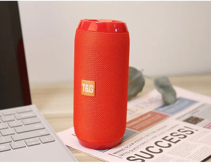 Red portable speaker on a desk with a laptop and newspaper
