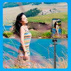 Woman in a striped dress standing by a lake with a phone holder displaying her reflection.