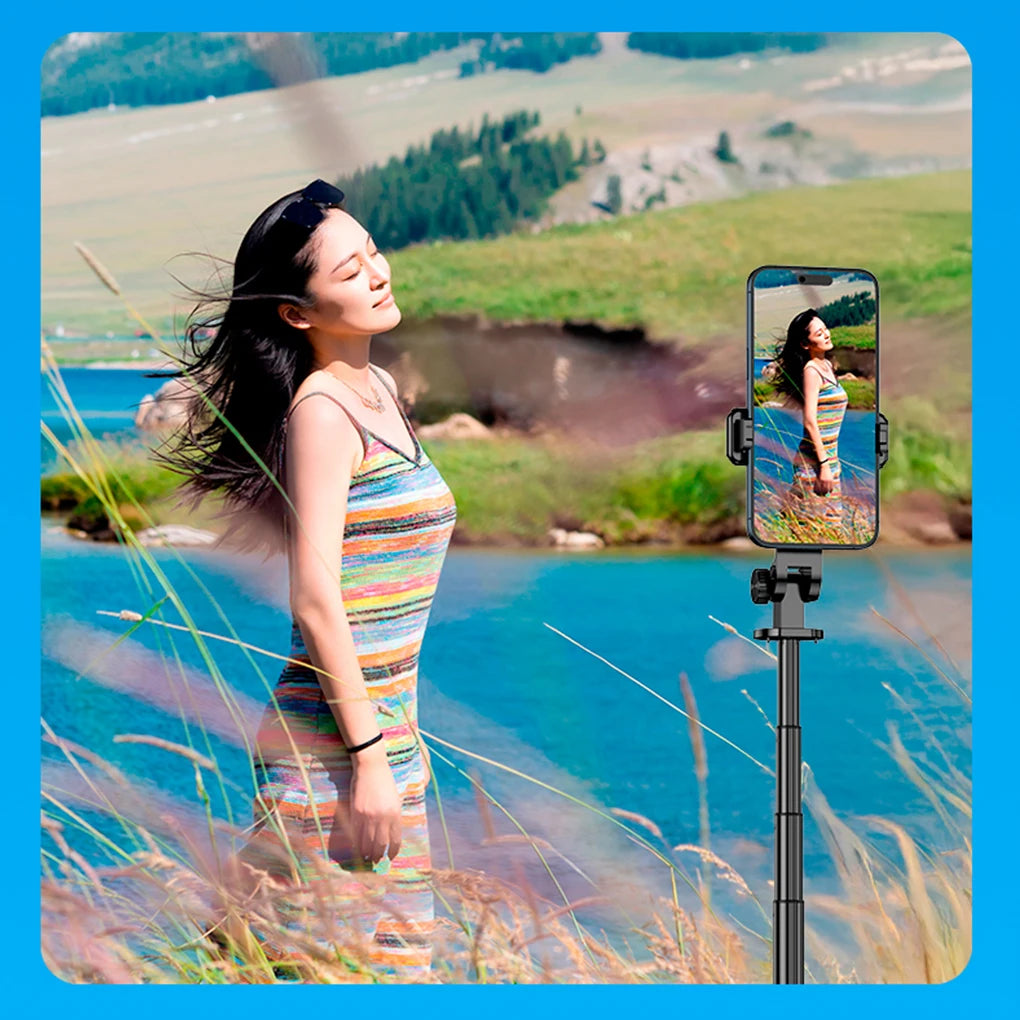 Woman in a striped dress standing by a lake with a phone holder displaying her reflection.