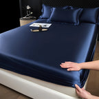 Navy blue satin sheet set being fitted onto a bed in a bedroom setting.
