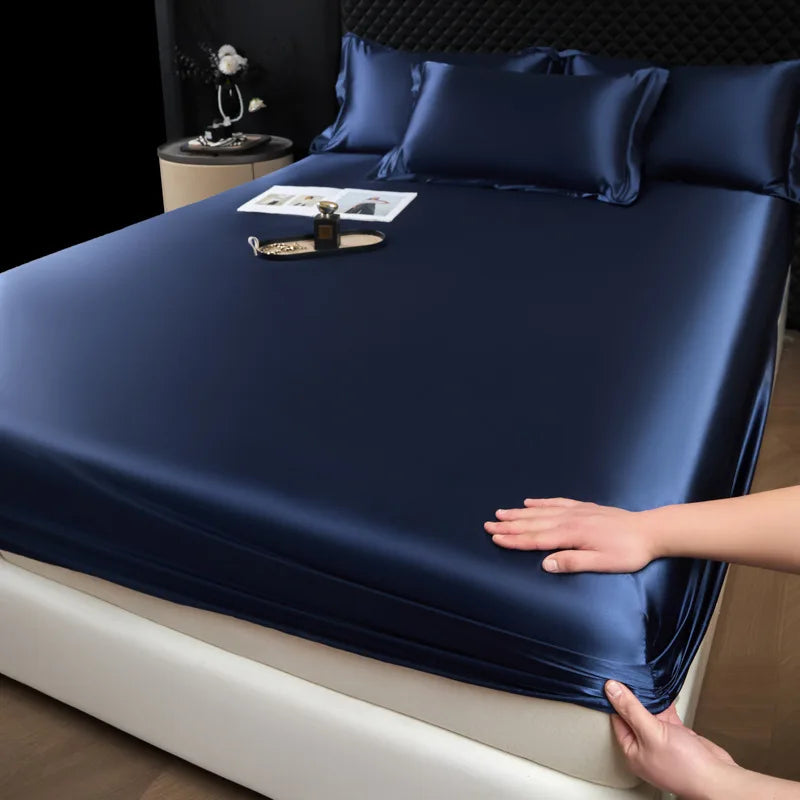 Navy blue satin sheet set being fitted onto a bed in a bedroom setting.
