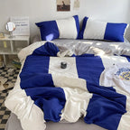 Blue and white bedding set on a bed in a room with a mirror and desk.