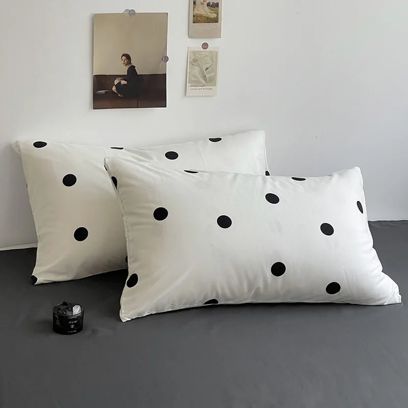 Two white pillows with black polka dots on a gray surface, with a light gray wall and framed picture in the background.