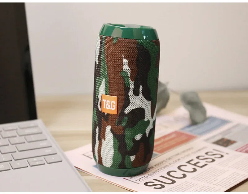 Camouflage-patterned portable speaker with TGG logo on a desk