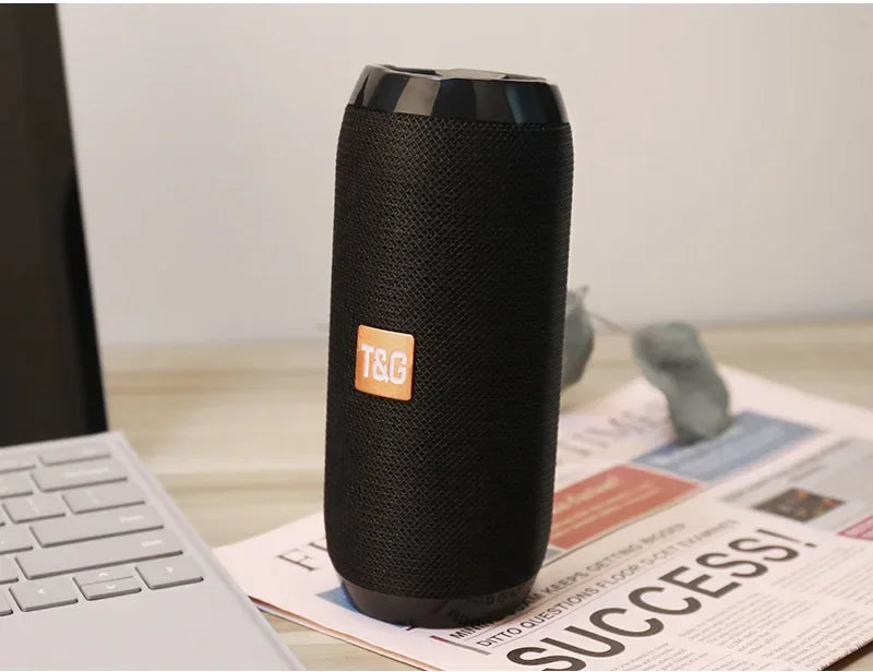 Black portable speaker with T&G logo on a desk with newspaper