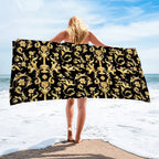 Person holding a large black and gold patterned towel on a beach