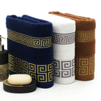 Three folded towels with geometric patterns in navy, white, and brown, accompanied by a bar of soap and a black container.