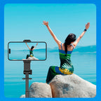 Woman on a rock by the sea with a phone holder showing her on screen.