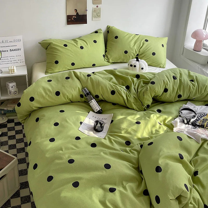 Green polka dot bedding set on a bed in a room with a small table and lamp.