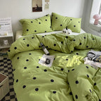 Green polka dot bedding set on a bed in a room with a small table and lamp.