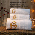 Set of white towels with gold embroidery on a wooden surface.